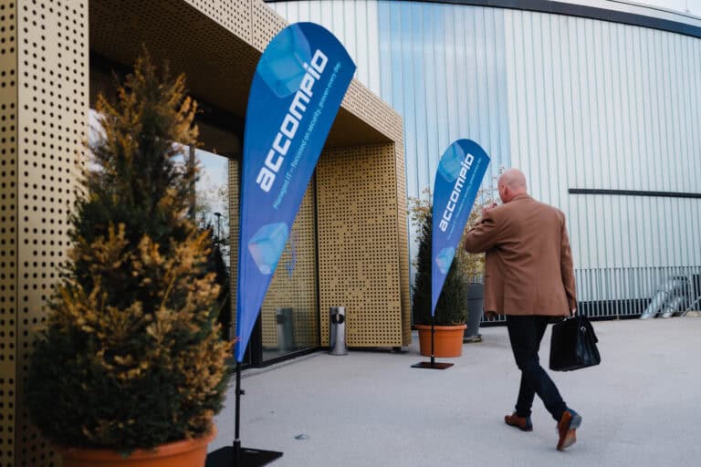 Mann bei accompio IT-Services Event mit Firmenflaggen im Außenbereich.